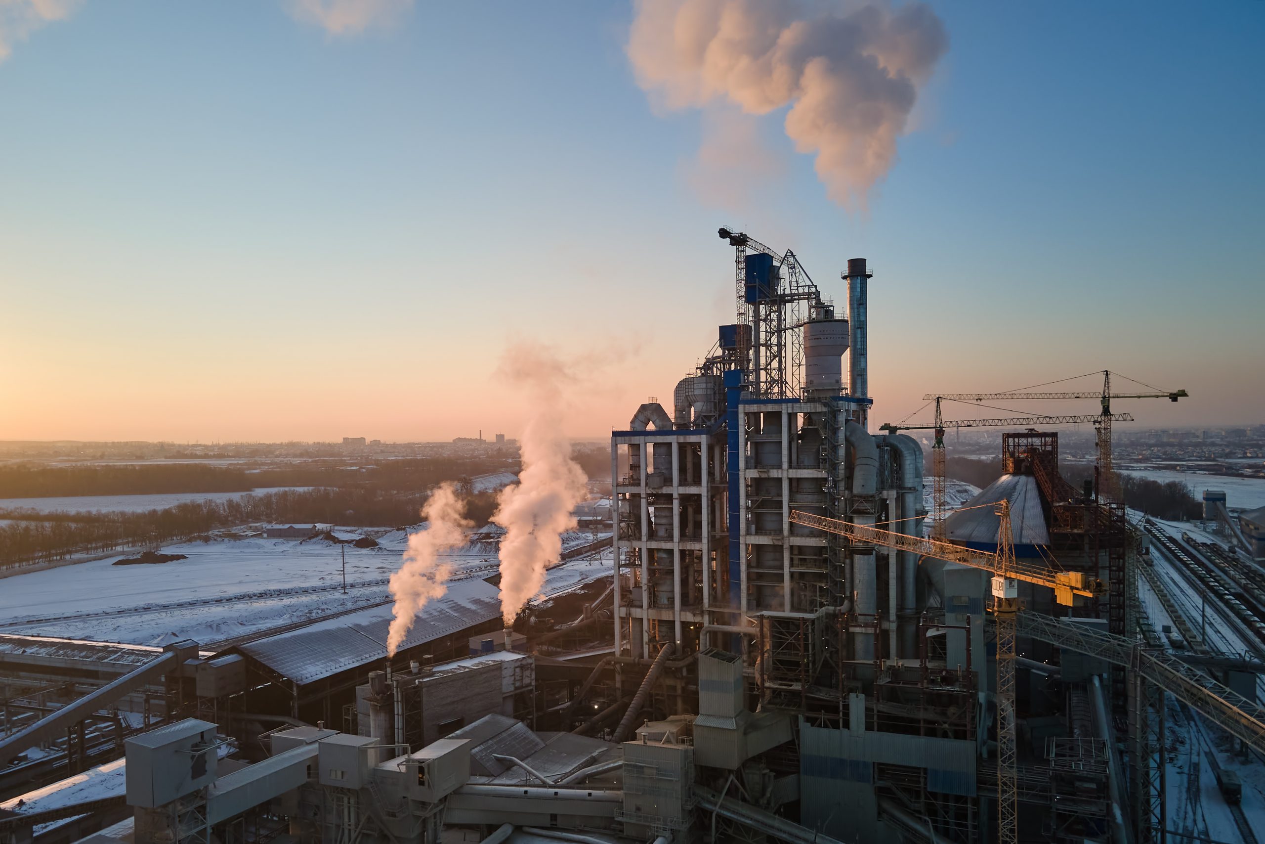 Aerial view of cement factory with high concrete plant structure and tower crane at industrial production area in evening. Manufacture and global industry concept